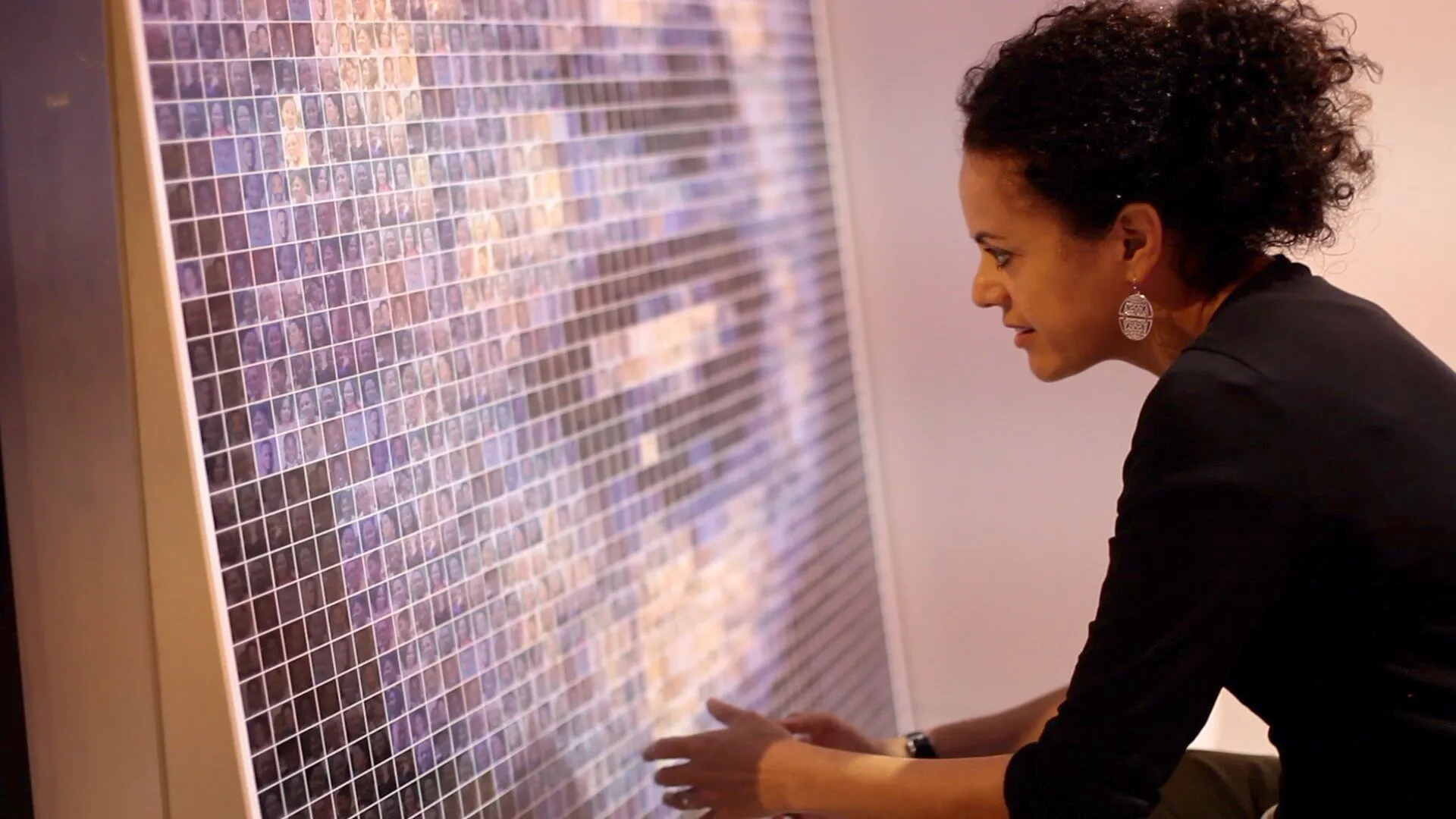 The artist looking closely at the photo-mosaic wall made up of hundreds of small portrait photographs