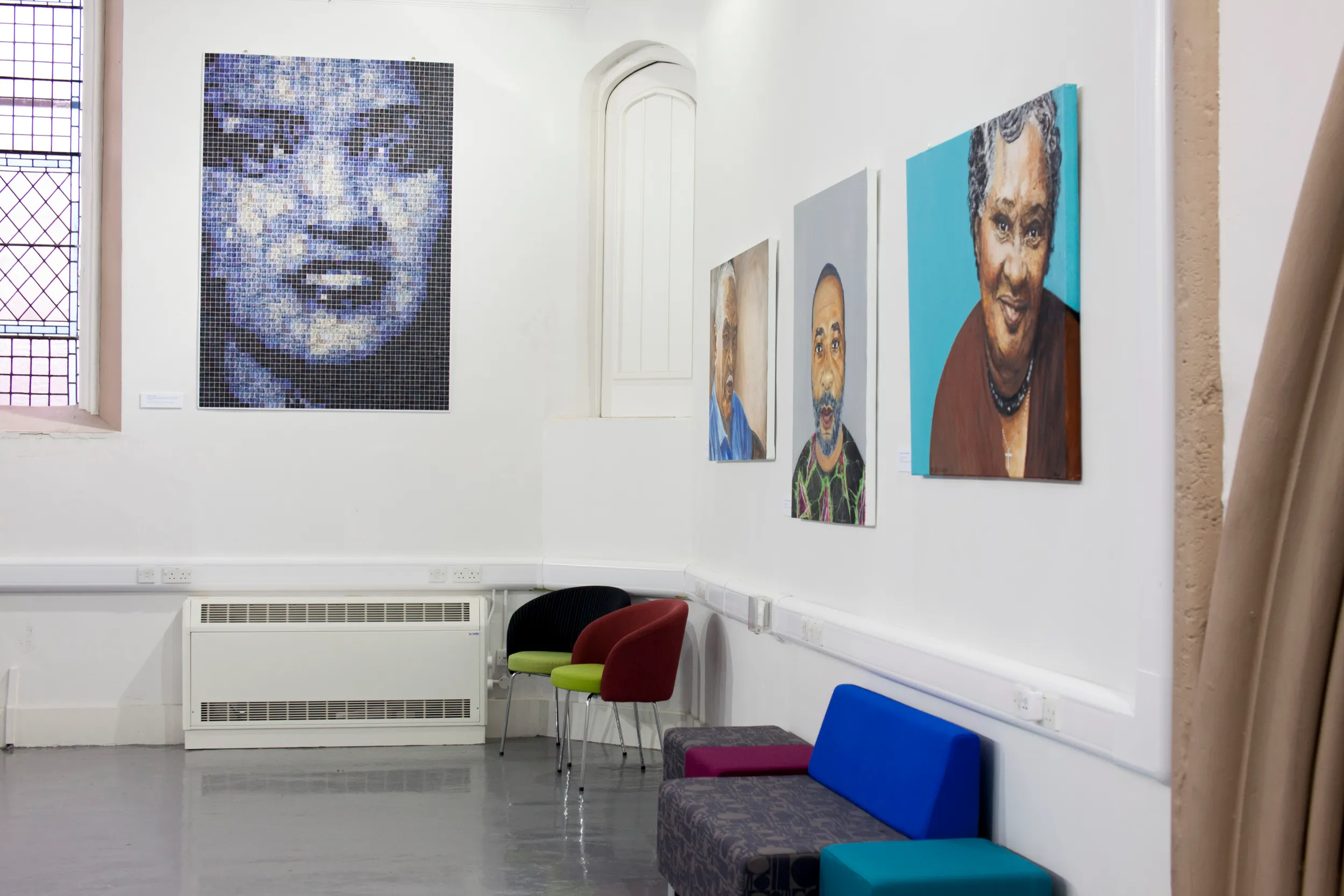 Gallery corner with a photo-mosaic portrait of Henrietta Lacks on one wall and painted portraits of her sons and a granddaughter on the adjoining wall