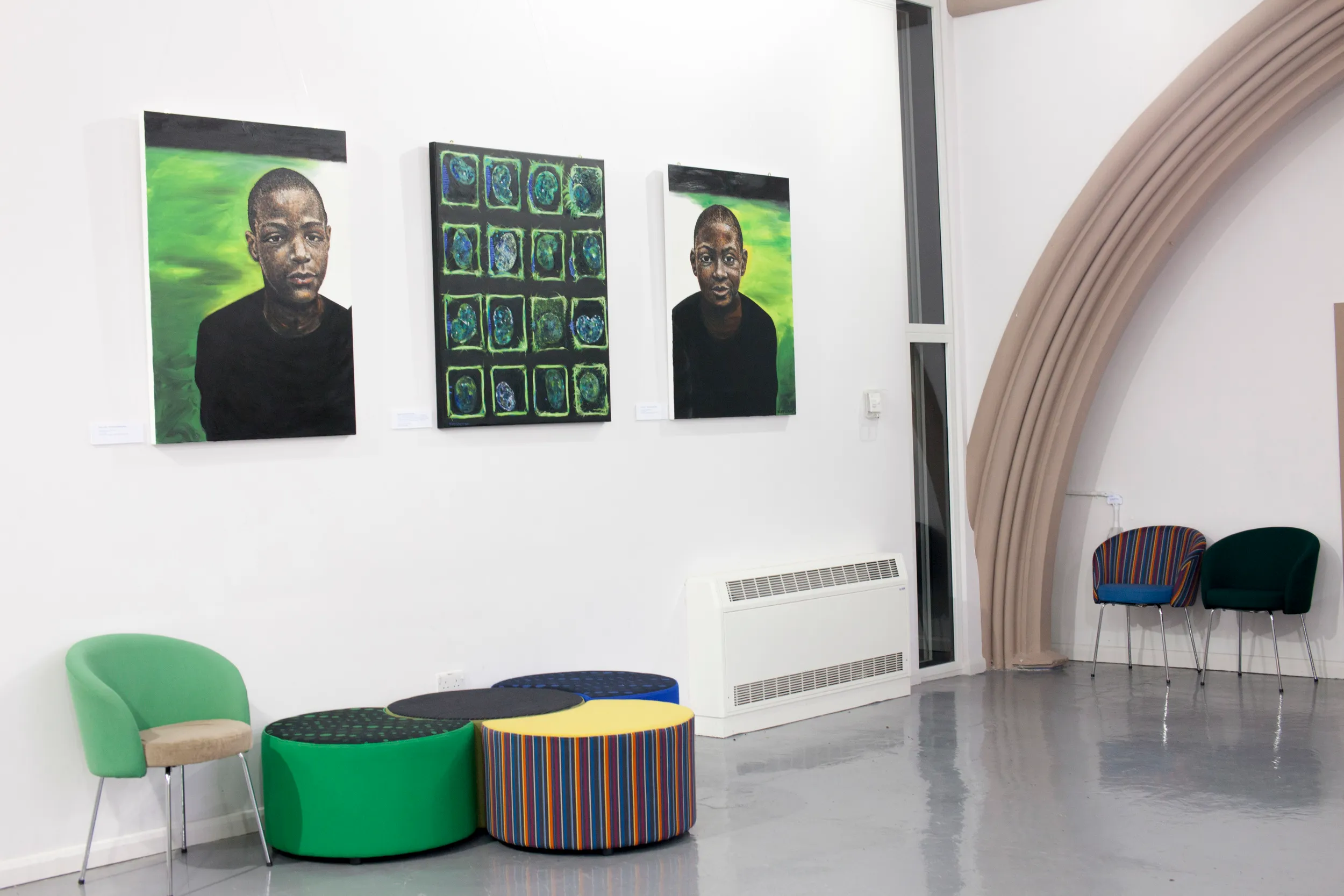 Three painted portraits of young men against green backgrounds, hung alongside a grid painting of cell-like circular forms