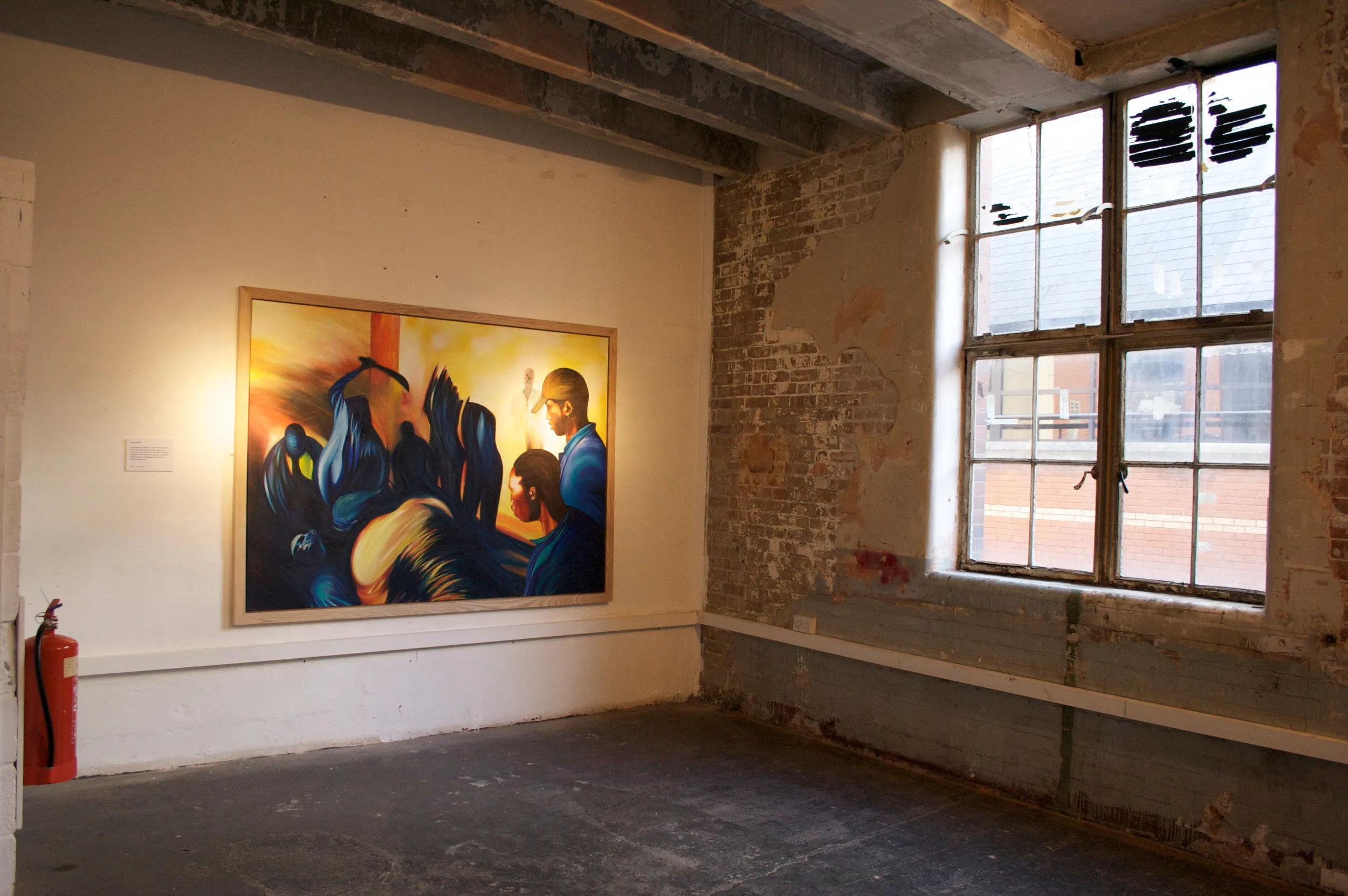 Large abstract painting of dark blue swirling draped forms and silhouetted figures under a golden sky, with a man in a cap looking on in the gallery