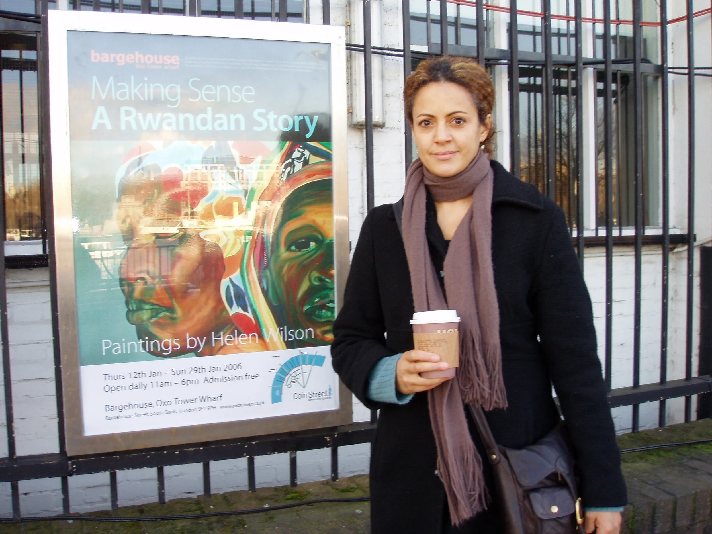 The artist Helen Wilson Roe standing beside the exhibition poster for Making Sense: A Rwandan Story outside the Bargehouse, Oxo Tower Wharf