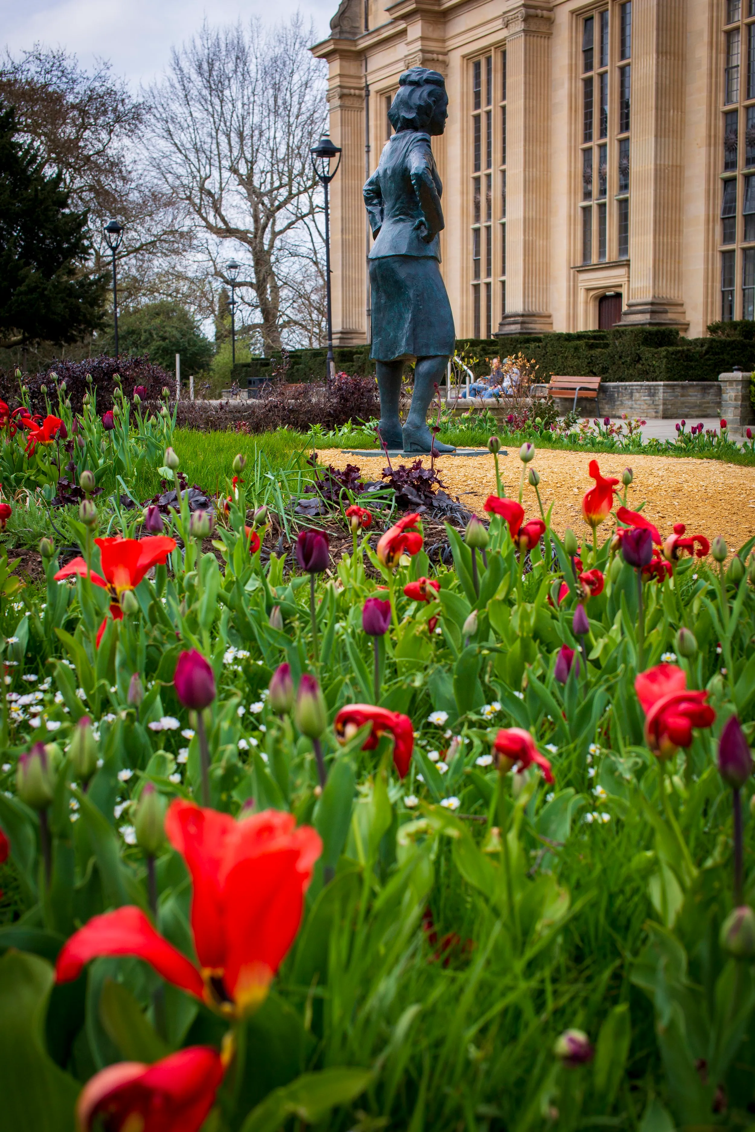 The Henrietta Lacks statue seen from a distance beside the Wills Memorial Building, framed by red tulips