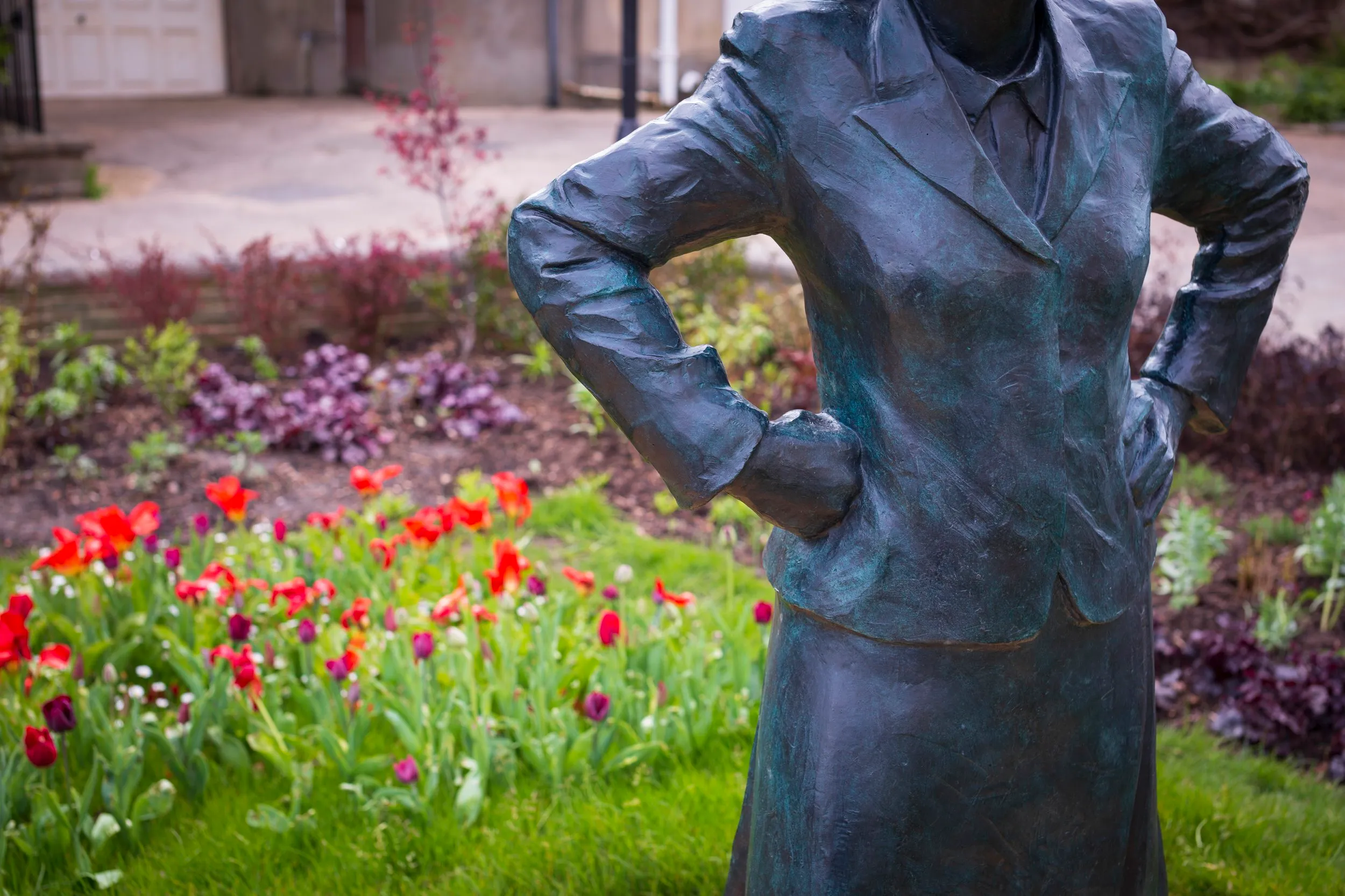 Close-up of the statue's jacket and hands resting on its hips, with flower beds behind