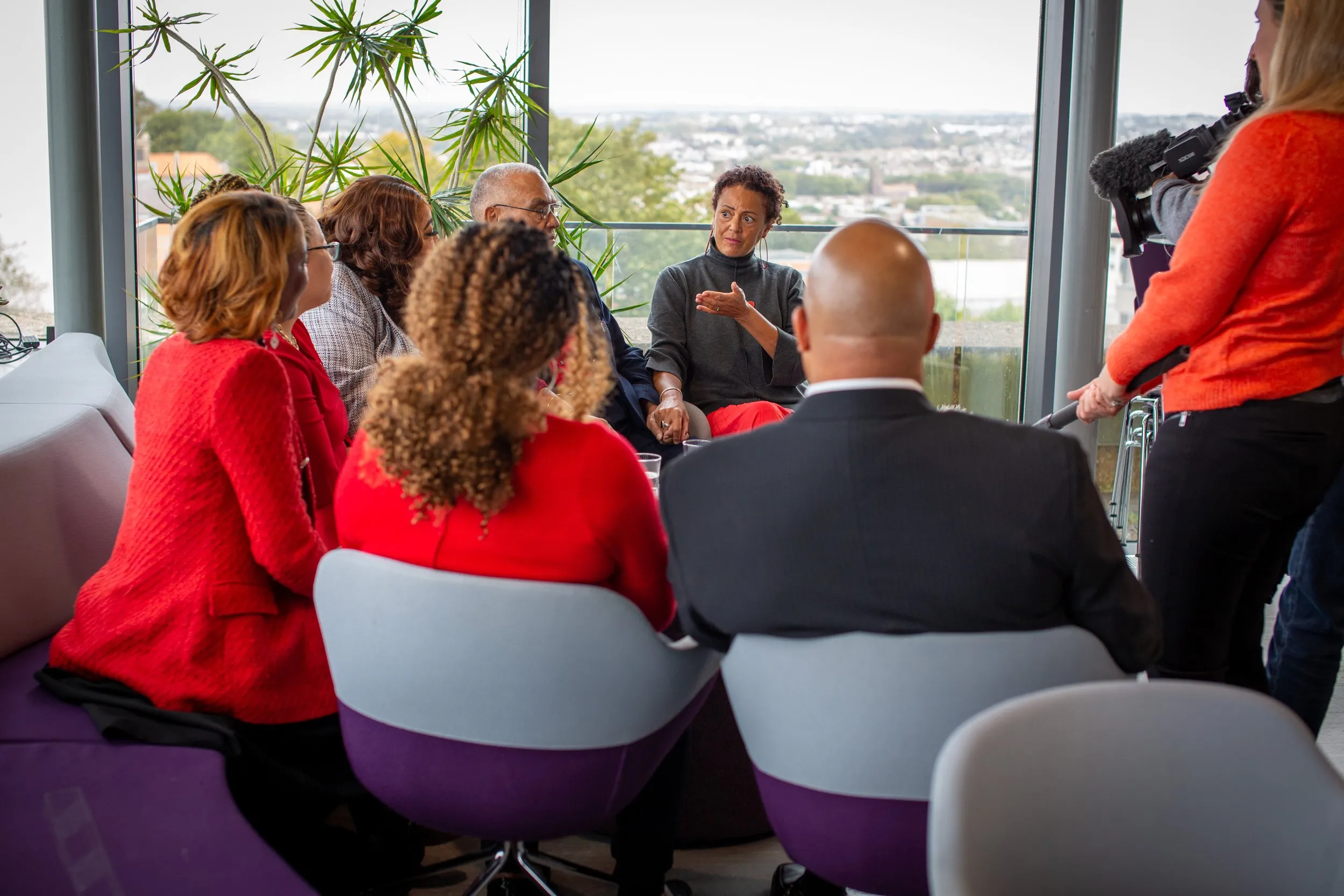 Helen Wilson Roe speaking to a seated group at the unveiling event, with a camera operator filming and a view over Bristol behind them