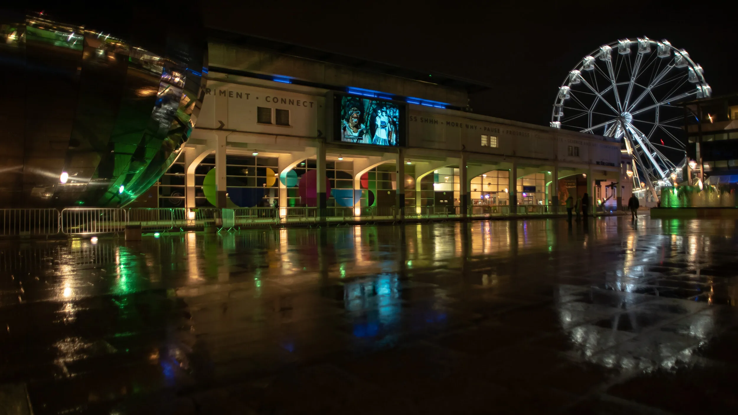 Night view of Millennium Square with a painting of two figures in patterned clothing shown on the big screen