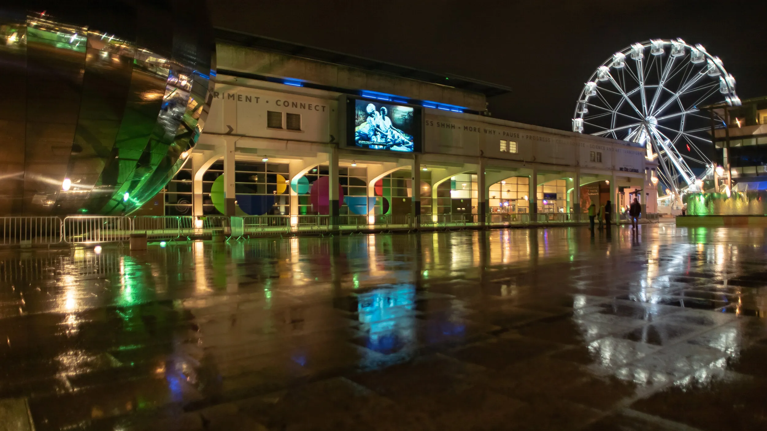 Night view of Millennium Square with a painting of two embracing figures in blue tones shown on the big screen