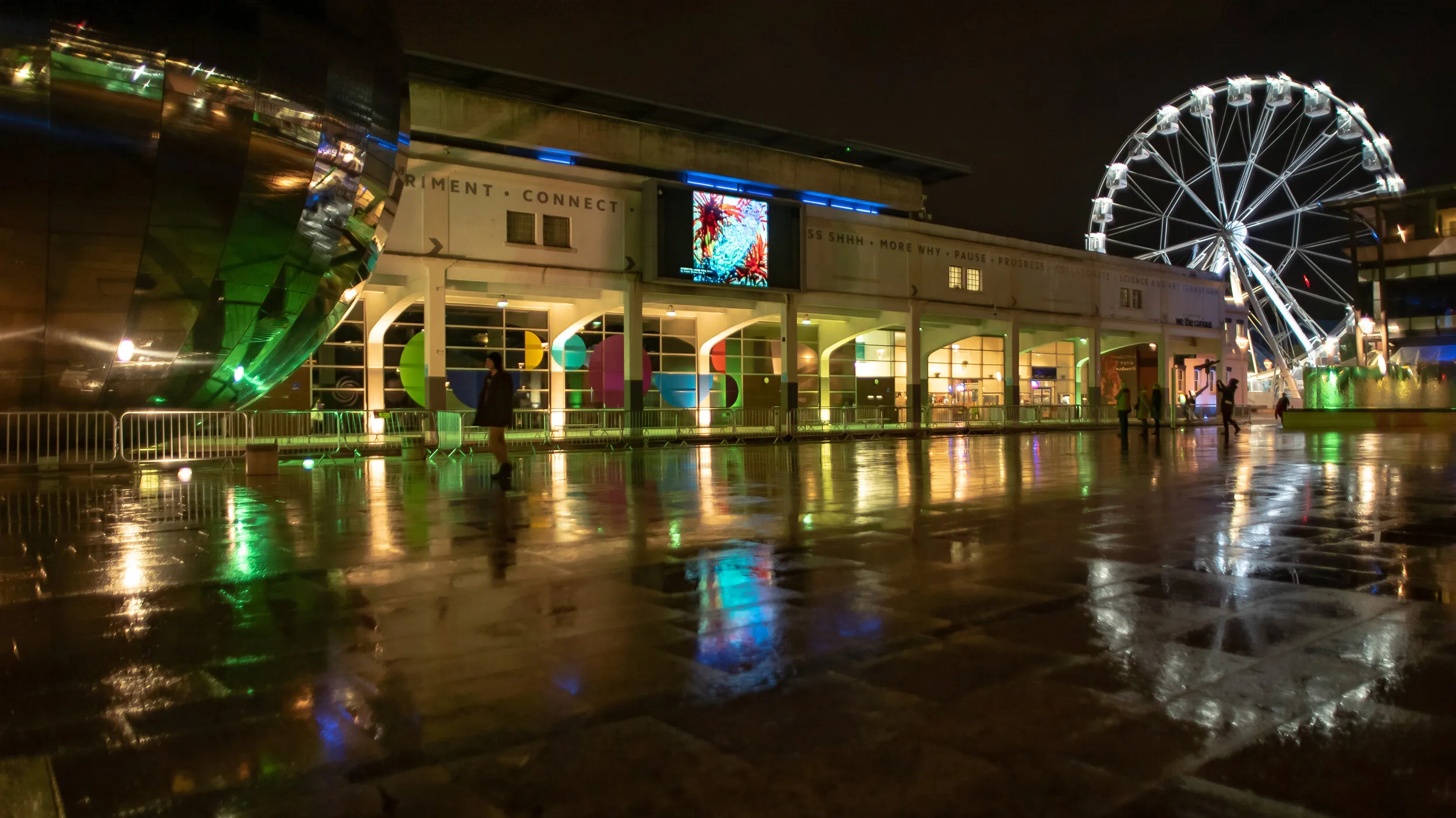 Night view of Millennium Square with an abstract image of red and blue organic forms shown on the big screen