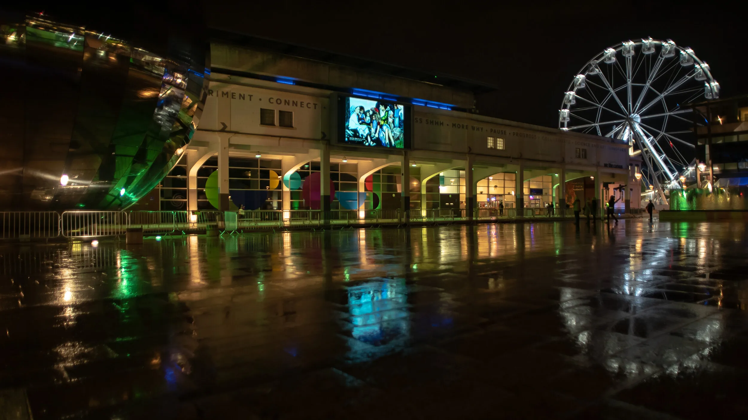 Night view of Millennium Square with a painting of several seated figures gathered together shown on the big screen